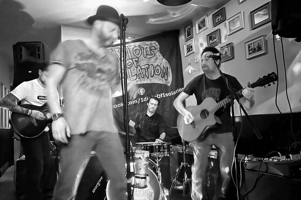 Idiots of Isolation playing in front of their banner: two guitarists, a drummer and the singer in a hat